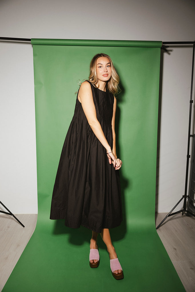 a sleeveless black midi dress with pleated details. the perfect cotton tank dress for weddings, baby showers, brunch dates, + casual outings.