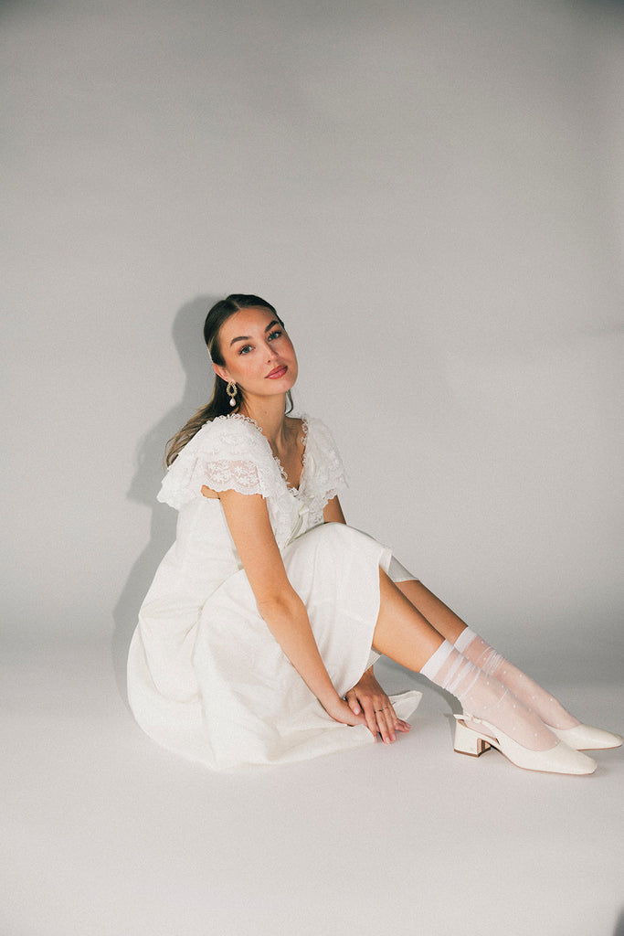 a white vintage-inspired midi dress with a lace ruffle neckline + bow detail. the perfect white dress for bridal showers, rehearsal dinners, + any special occasion.