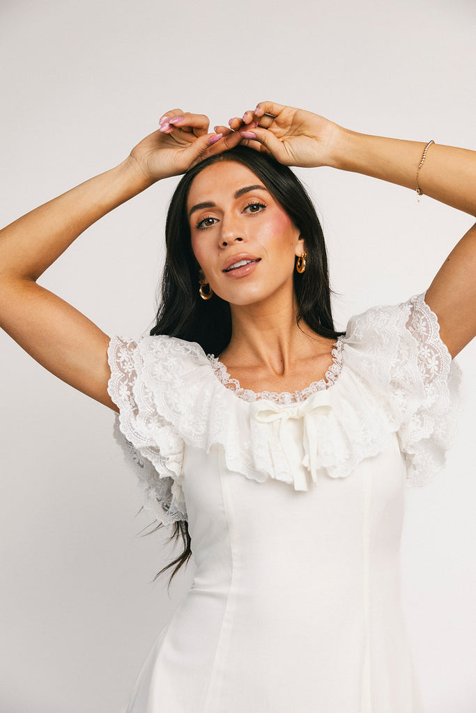a white vintage-inspired midi dress with a lace ruffle neckline + bow detail. the perfect white dress for bridal showers, rehearsal dinners, + any special occasion.