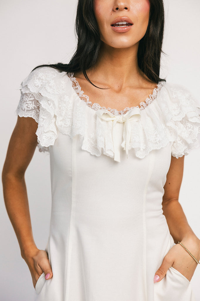 a white vintage-inspired midi dress with a lace ruffle neckline + bow detail. the perfect white dress for bridal showers, rehearsal dinners, + any special occasion.