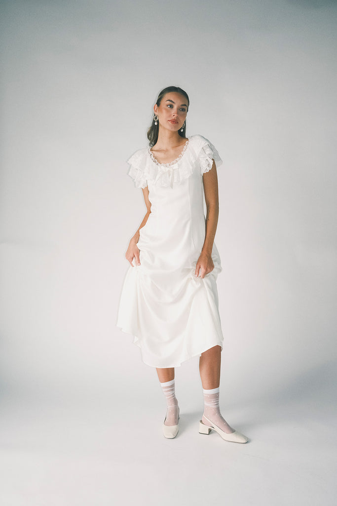a white vintage-inspired midi dress with a lace ruffle neckline + bow detail. the perfect white dress for bridal showers, rehearsal dinners, + any special occasion.
