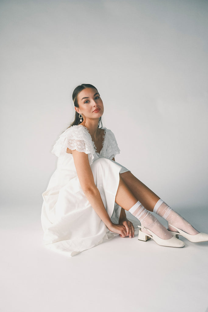 a white vintage-inspired midi dress with a lace ruffle neckline + bow detail. the perfect white dress for bridal showers, rehearsal dinners, + any special occasion.