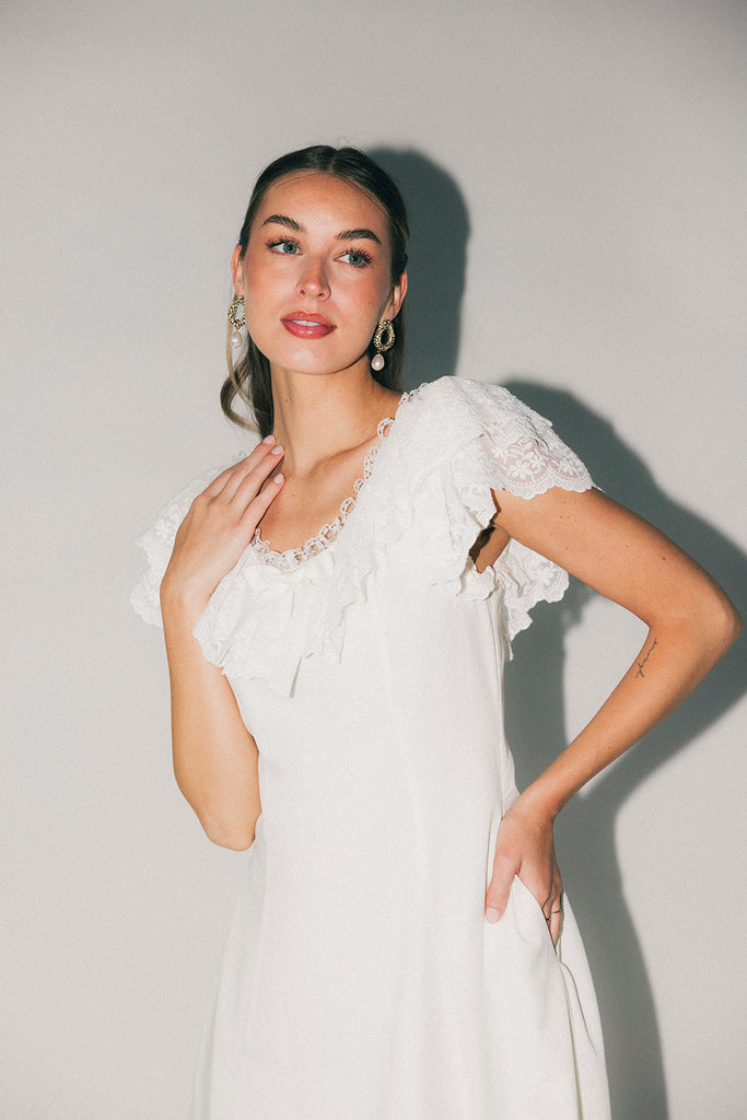 a white vintage-inspired midi dress with a lace ruffle neckline + bow detail. the perfect white dress for bridal showers, rehearsal dinners, + any special occasion.
