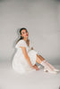 a white vintage-inspired midi dress with a lace ruffle neckline + bow detail. the perfect white dress for bridal showers, rehearsal dinners, + any special occasion.
