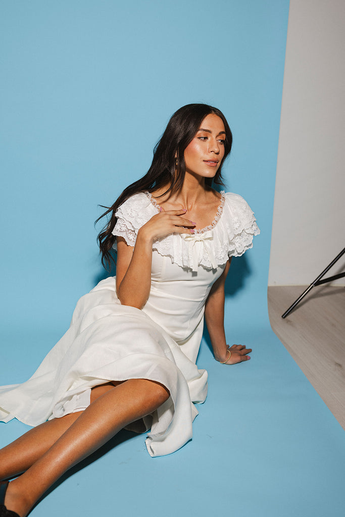 a white vintage-inspired midi dress with a lace ruffle neckline + bow detail. the perfect white dress for bridal showers, rehearsal dinners, + any special occasion.
