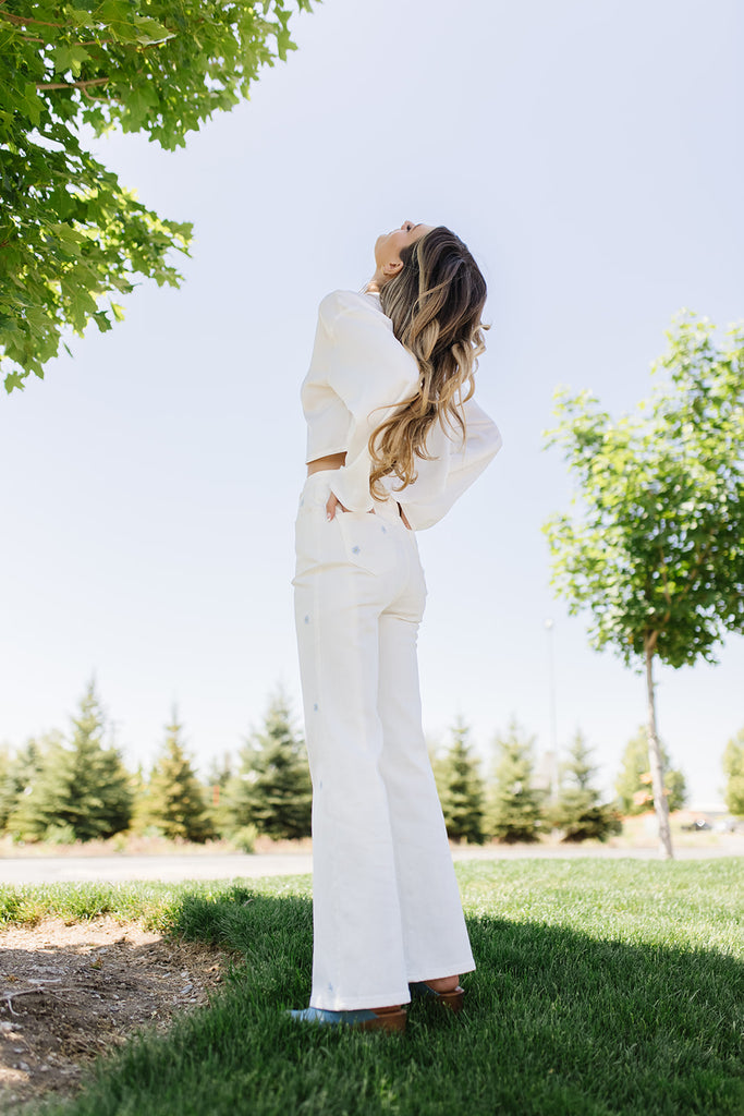 white denim with embroidered daisies, slight flare, one button zipper fly, pockets, and belt loops.